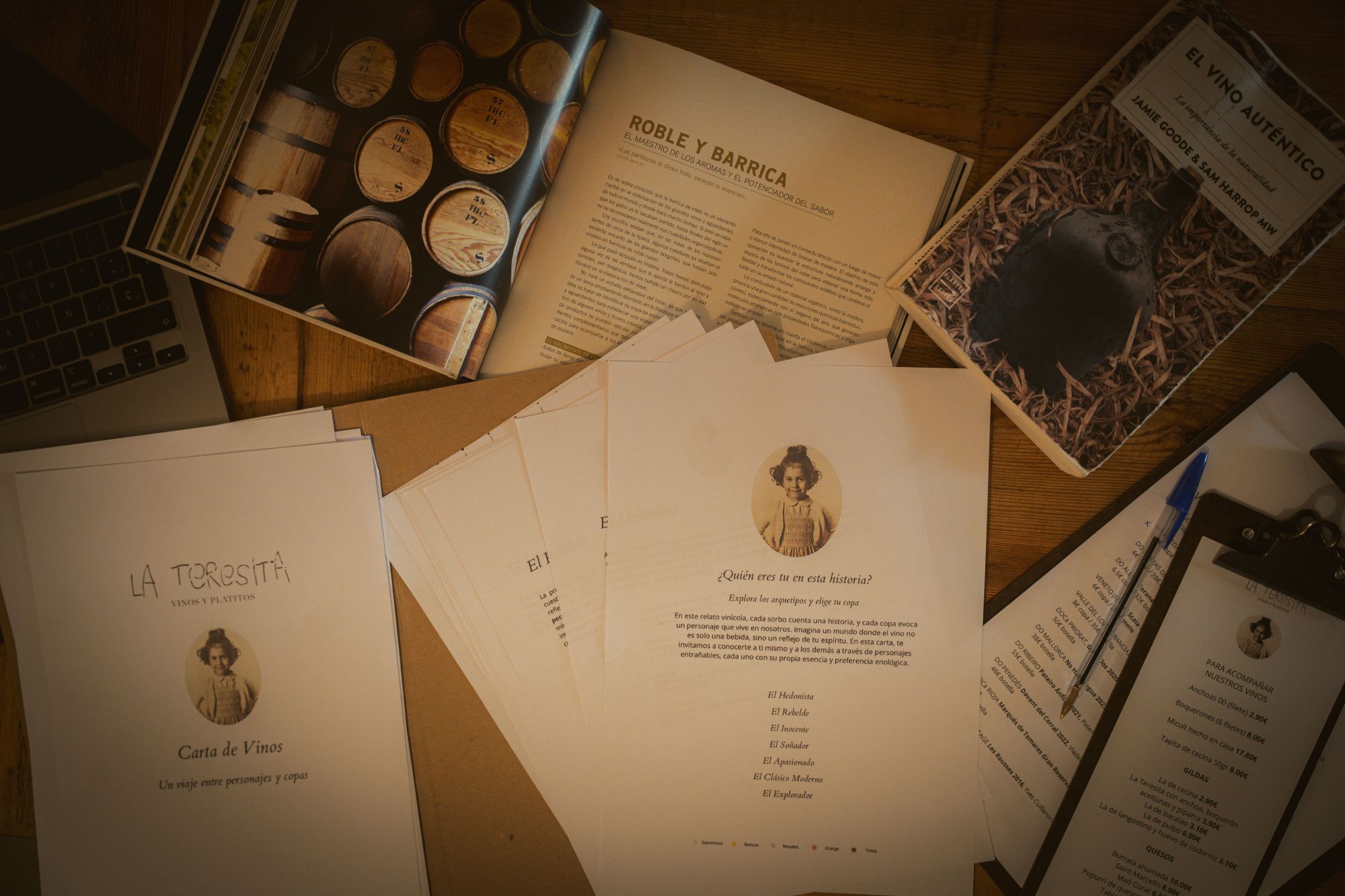 Cartas de vino impresas sobre una mesa de madera junto a libros de vino y notas de trabajo