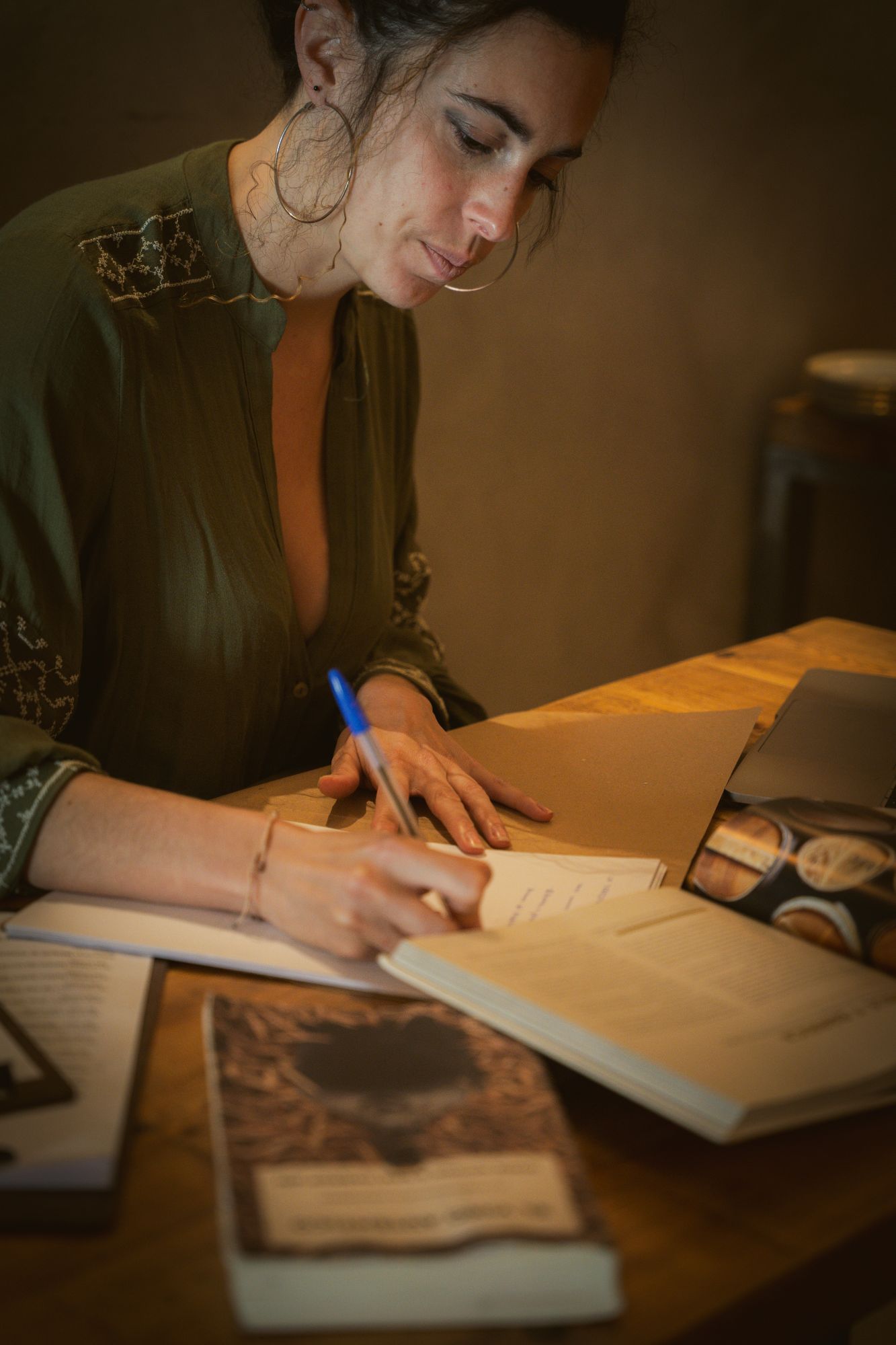 Sara escribiendo notas a mano rodeada de libros de vino